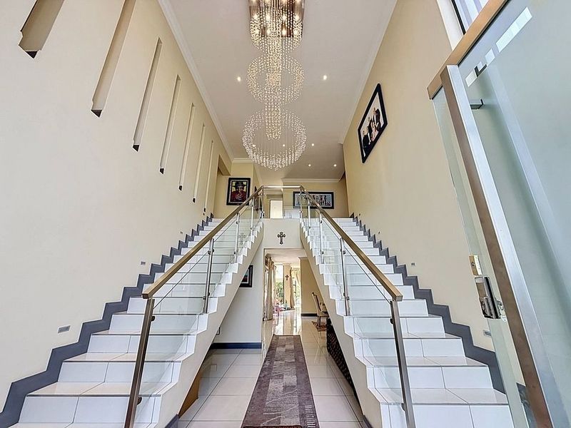 Grand entrance hall featuring a symmetrical double staircase with glass balustrades, tiled flooring, and a striking multi-tiered crystal chandelier.