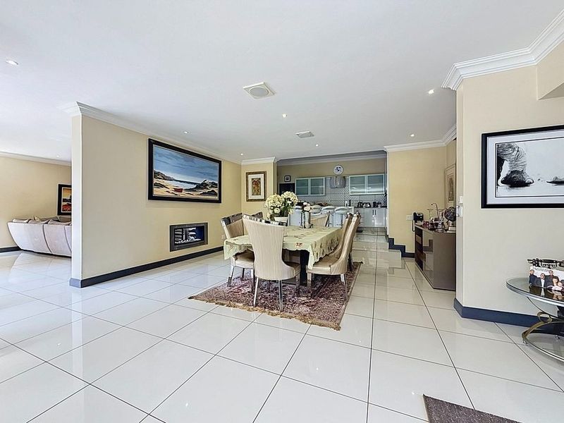 Spacious open-plan living and dining area featuring polished porcelain tiles, recessed lighting, crown molding, and a sleek built-in fireplace, flowing into a modern kitchen.