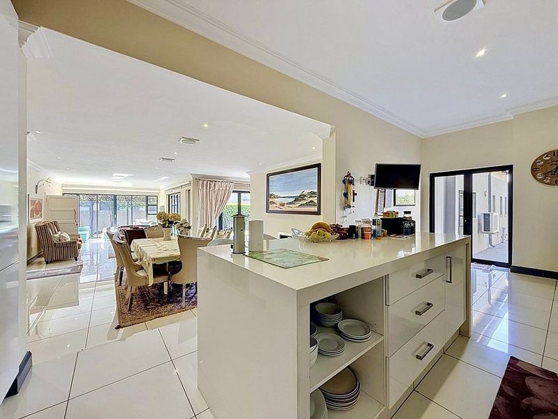 Spacious open-plan living and kitchen area featuring a central island, modern tiled flooring, and large sliding doors leading to the outdoor space.