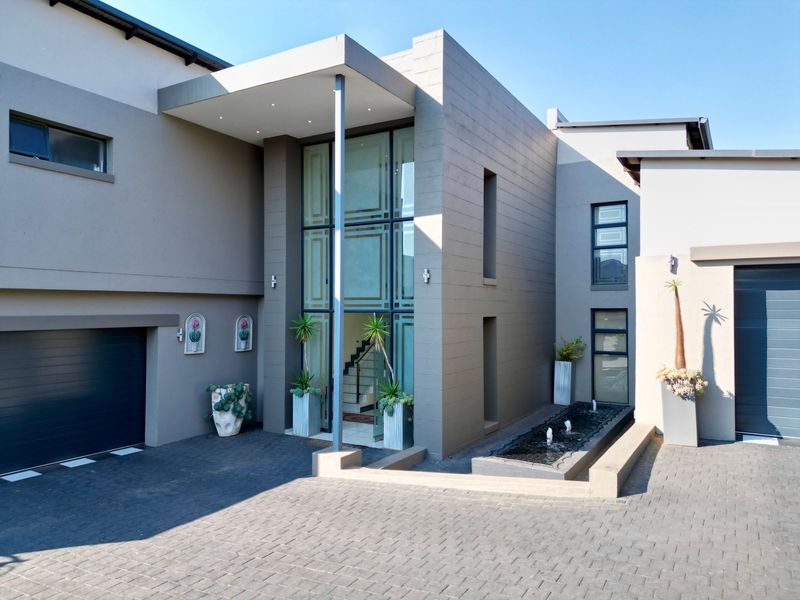 Modern double-story residence featuring a striking full-height glass entrance, integrated water feature, paved driveway, and double garage.
