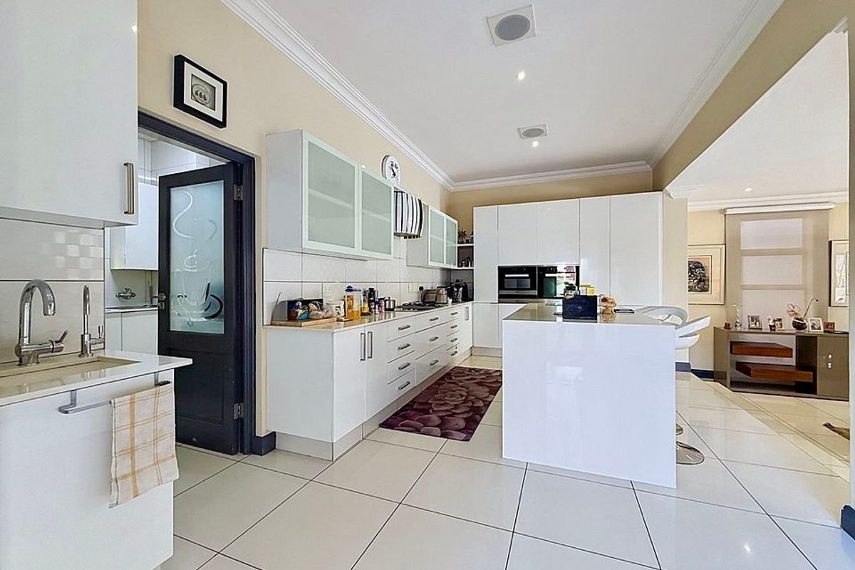 Modern kitchen featuring white cabinetry, a central island, built-in appliances, and tiled flooring, with an adjacent scullery area.