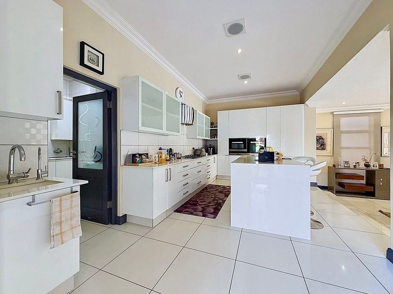 Modern kitchen featuring white cabinetry, a central island, built-in appliances, and tiled flooring, with an adjacent scullery area.