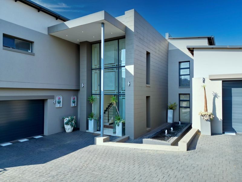 Modern double-storey residence featuring a striking double-volume glass entrance, integrated water feature, paved driveway, and double garage.