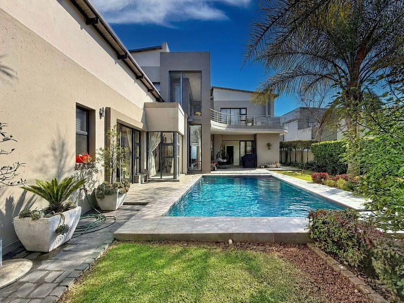 A well-maintained rear garden featuring a modern swimming pool, tiled patio area, and a balcony overlooking the outdoor space.