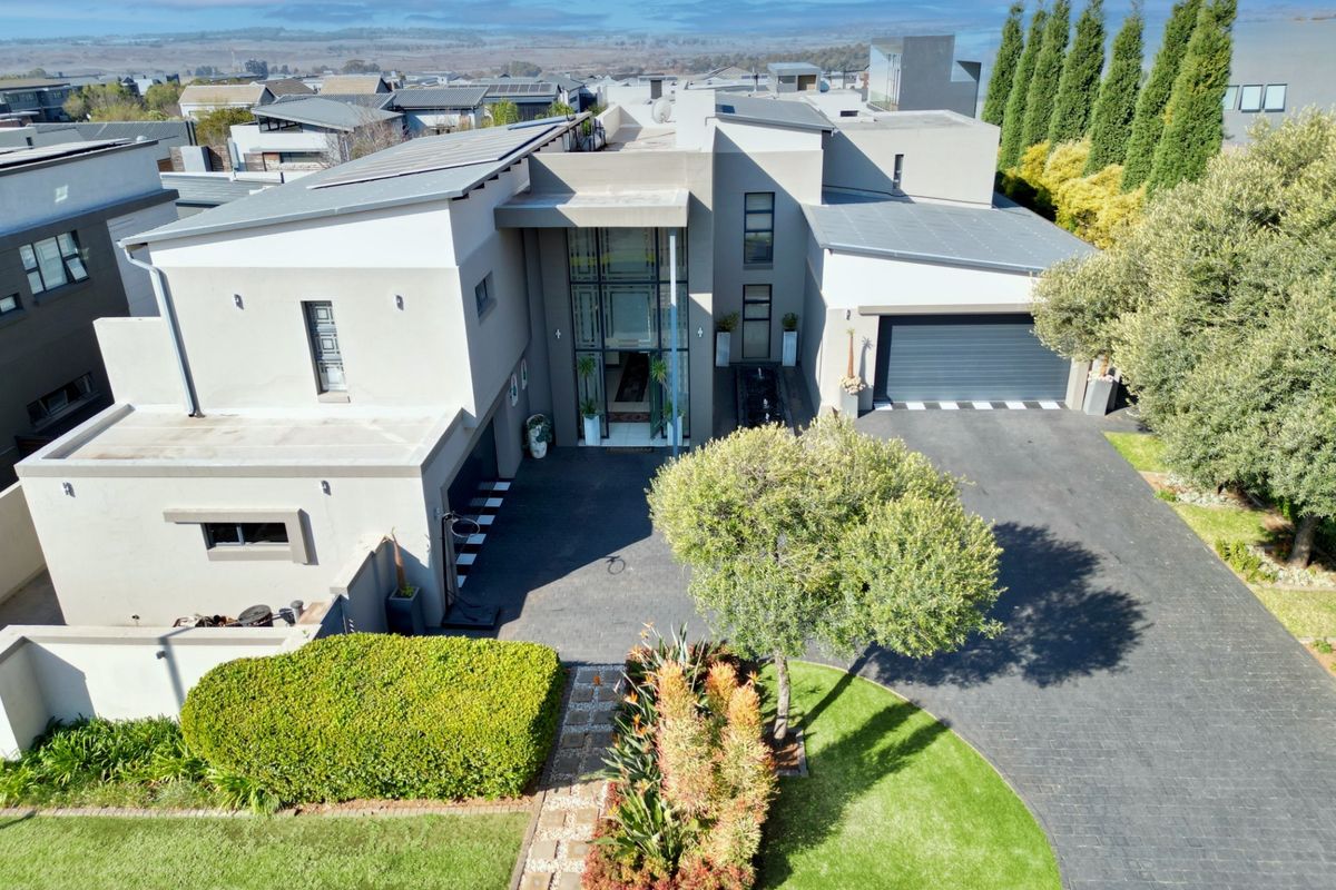 Aerial view of a modern multi-level residence featuring a paved driveway, double garage, solar panels, and a well-maintained landscaped garden.