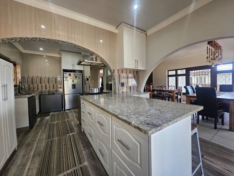 Spacious open-plan kitchen featuring a large granite island, ample built-in cabinetry, and elegant archways connecting to the dining area.