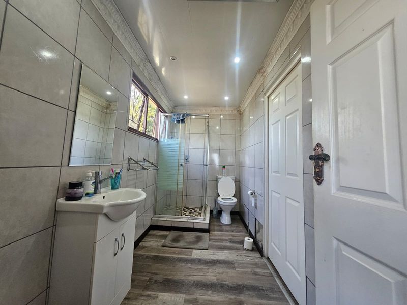 A functional bathroom featuring a shower enclosure, vanity cabinet, and tiled wall finishes with recessed lighting.
