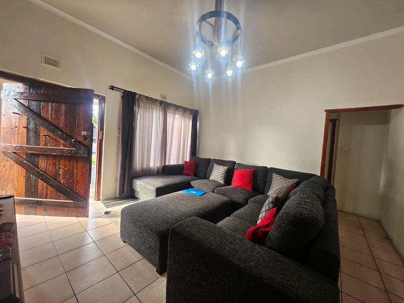 A living room featuring tiled flooring, a rustic timber entrance door, and a decorative pendant light fixture.