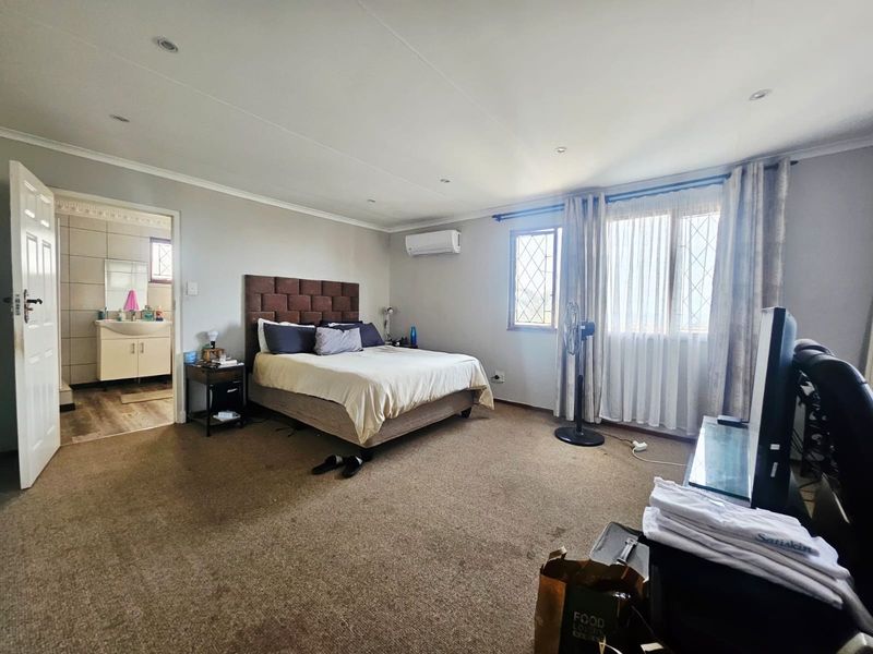 Spacious bedroom featuring neutral walls, carpeted flooring, recessed lighting, a wall-mounted air conditioner, and direct access to an en-suite bathroom.
