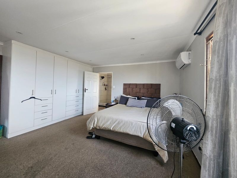 Spacious bedroom featuring extensive built-in cabinetry, neutral carpeting, recessed lighting, and a wall-mounted air conditioning unit with an adjoining en-suite bathroom.