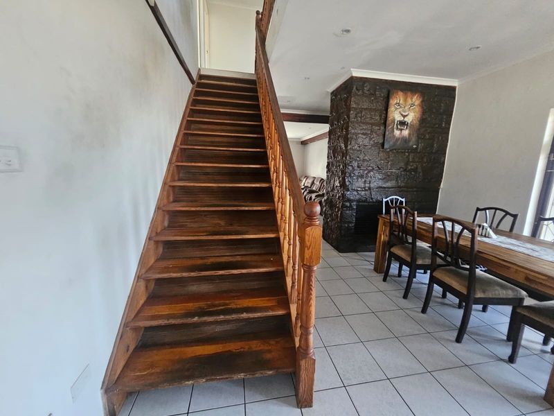 Open plan living area featuring a prominent wooden staircase, stone-clad fireplace, and neutral tiled flooring throughout the space.