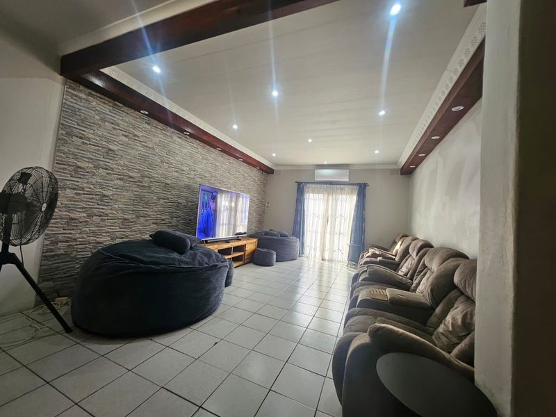 Spacious living room featuring a stone-clad accent wall, exposed timber ceiling beams, recessed lighting, and tiled flooring with direct access to the outdoors.