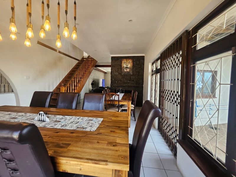 Open-plan dining area featuring a stone fireplace, wooden staircase, tiled flooring, and decorative pendant lighting, with access to an outdoor patio area.