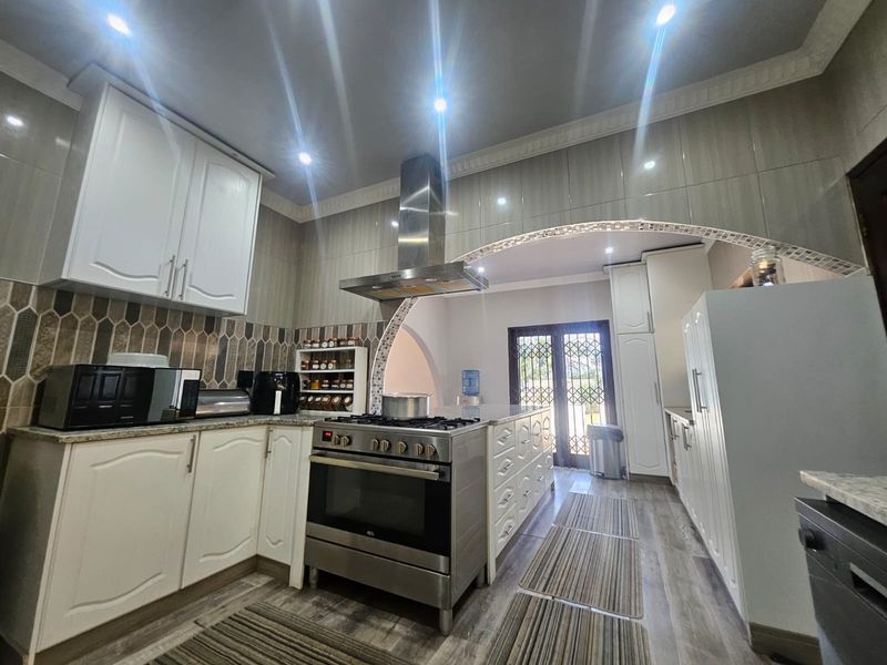 Modern kitchen featuring white cabinetry, granite countertops, stainless steel gas stove with extractor fan, and decorative tiled backsplash under an arched ceiling detail.