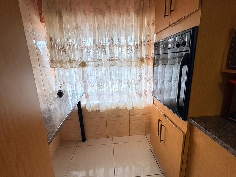 A compact kitchen area featuring built-in oven, laminate cabinetry, tiled splashbacks, and tiled flooring.