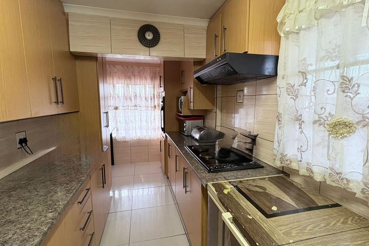 A functional galley-style kitchen featuring laminate cabinetry, granite countertops, tiled flooring, and a built-in hob with an extractor fan.