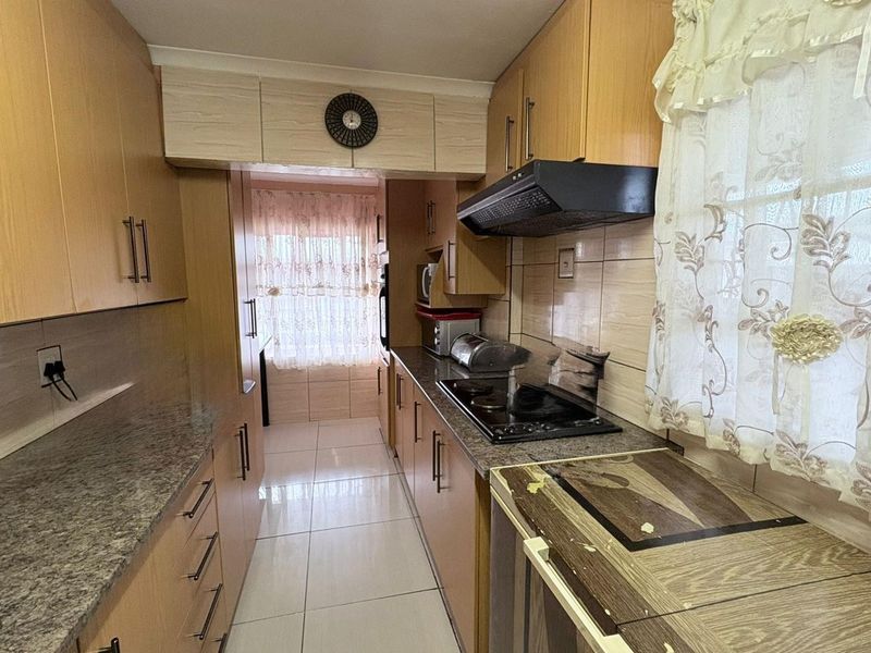A functional galley-style kitchen featuring laminate cabinetry, granite countertops, tiled flooring, and a built-in hob with an extractor fan.