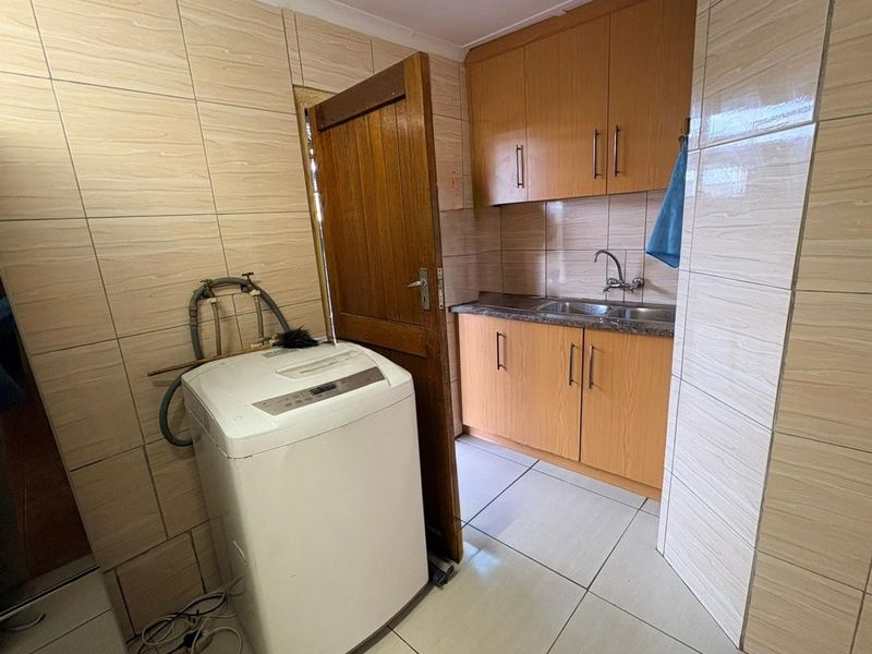A functional laundry area featuring built-in wooden cabinetry, laminate countertops, a stainless steel sink, and full-height wall tiling.