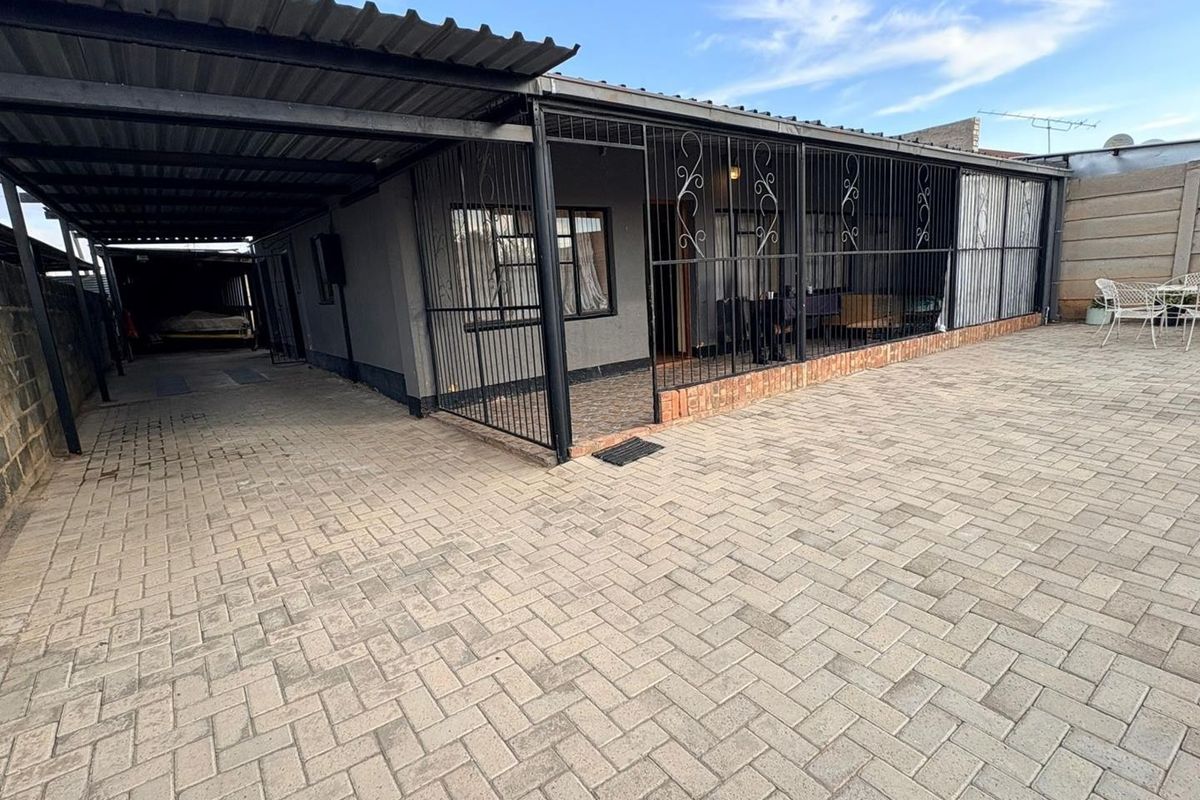 Rear exterior view featuring a paved driveway, covered carport area, and secure metal gate enclosures along the building facade.