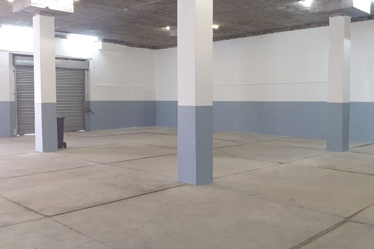 Spacious industrial utility area featuring exposed concrete ceilings, structural columns, and a secure roller shutter door, suitable for storage or workshop use.