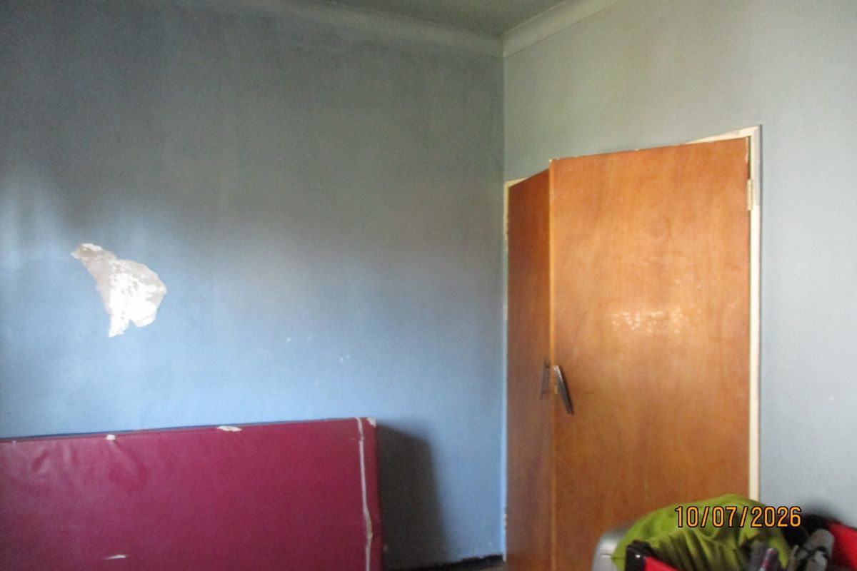 A bedroom featuring a built-in wooden wardrobe and coving, currently requiring cosmetic attention to the wall surfaces.