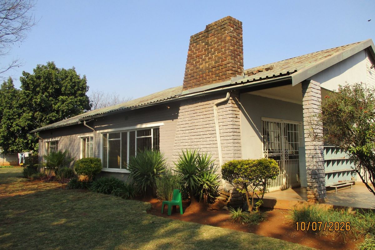 Rear view of the house featuring a prominent brick chimney, covered patio area, and established garden surroundings.