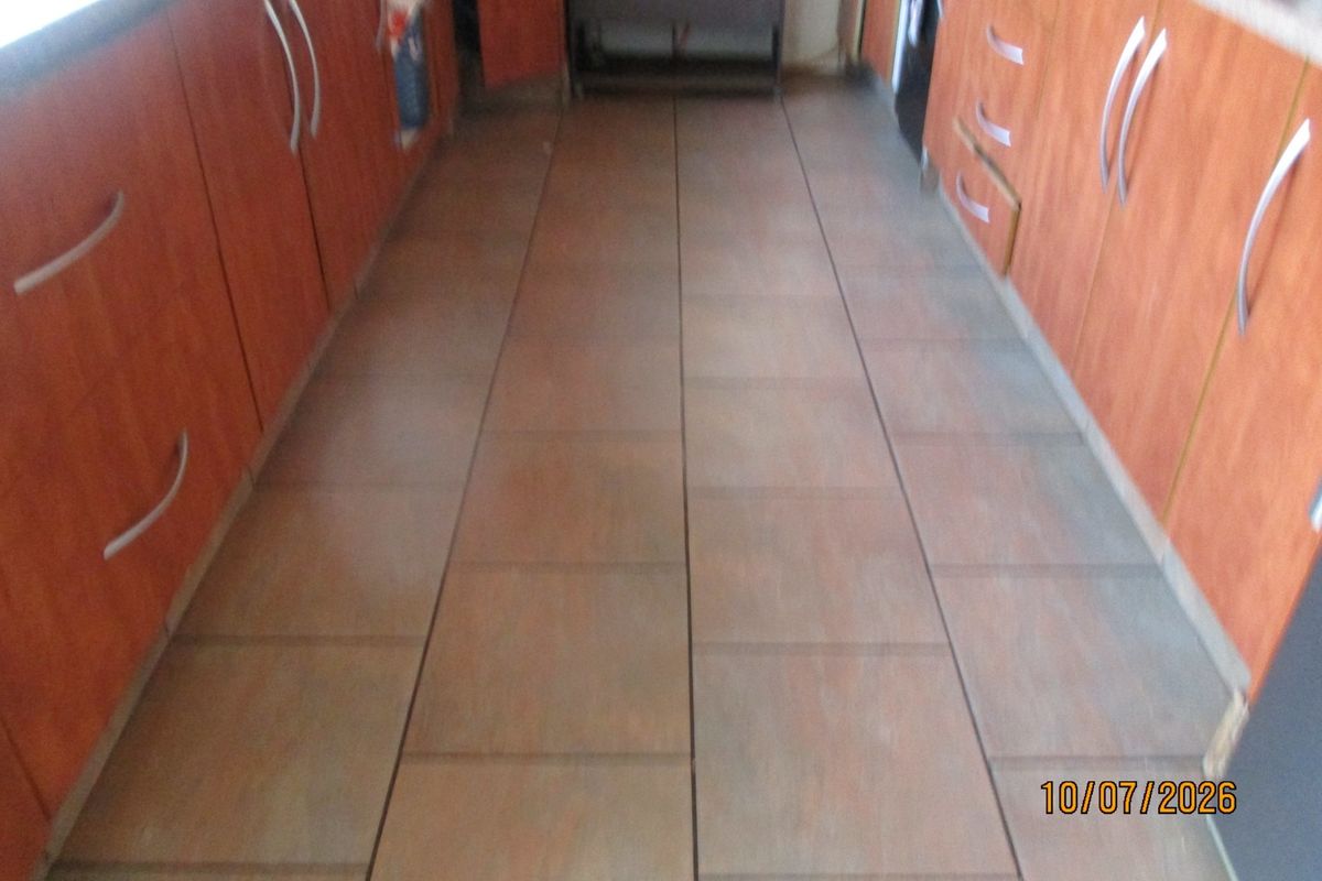 A galley-style kitchen featuring wood-look laminate cabinetry and tiled flooring, currently in need of cosmetic updates to modernize the space.
