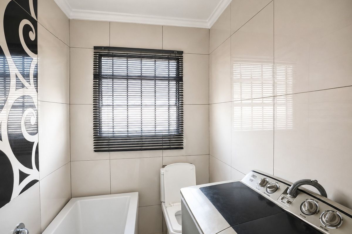 A compact bathroom featuring floor-to-ceiling ceramic tiling, a built-in bathtub, and a toilet, finished with modern neutral tones and decorative accent tiles.