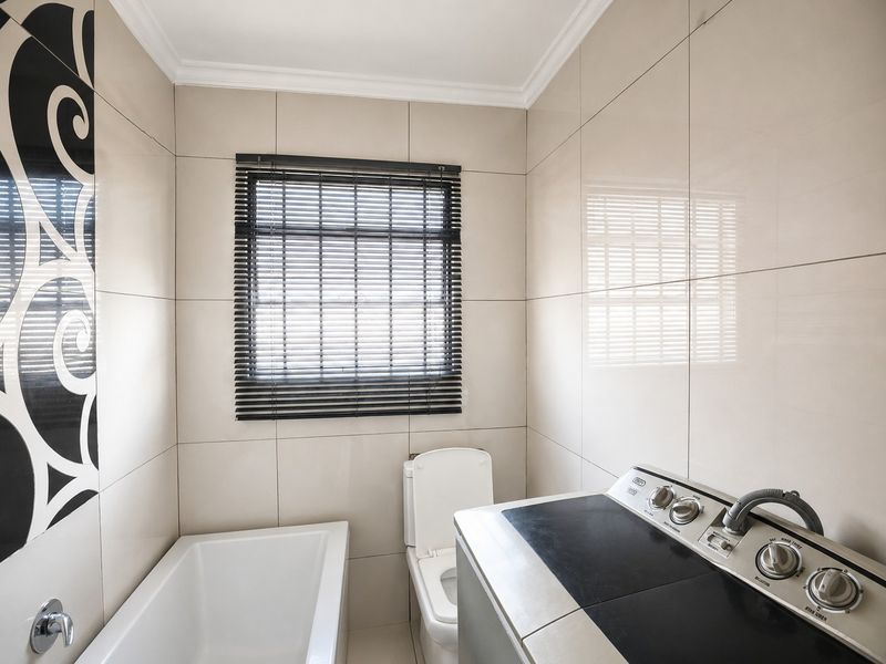 A compact bathroom featuring floor-to-ceiling ceramic tiling, a built-in bathtub, and a toilet, finished with modern neutral tones and decorative accent tiles.