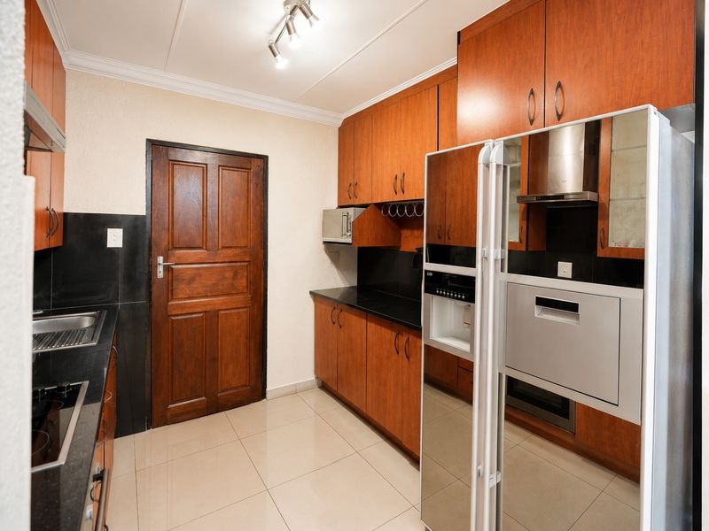 A functional kitchen featuring warm-toned wooden cabinetry, black granite countertops, integrated appliances, and neutral floor tiling.