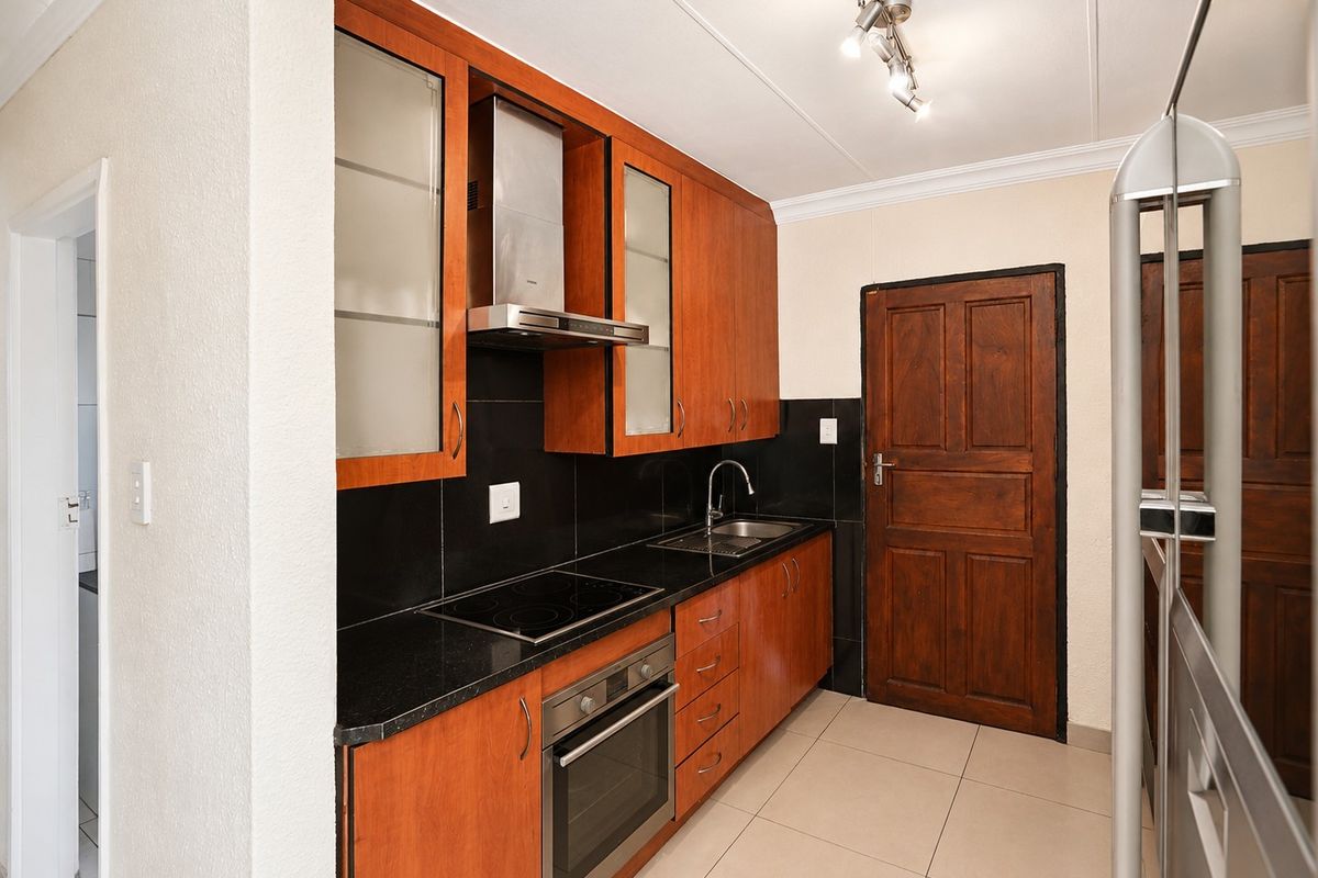 A functional kitchen featuring warm-toned wooden cabinetry, black granite countertops, integrated appliances, and tiled flooring.