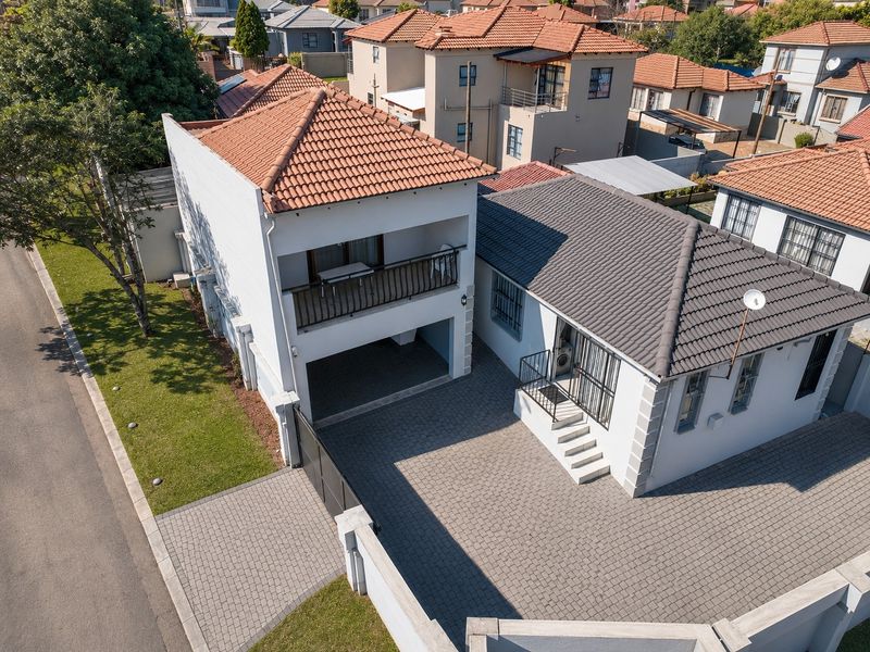 Aerial view of a residential property featuring a paved driveway, tiled roof, and a balcony, situated within a suburban neighborhood.