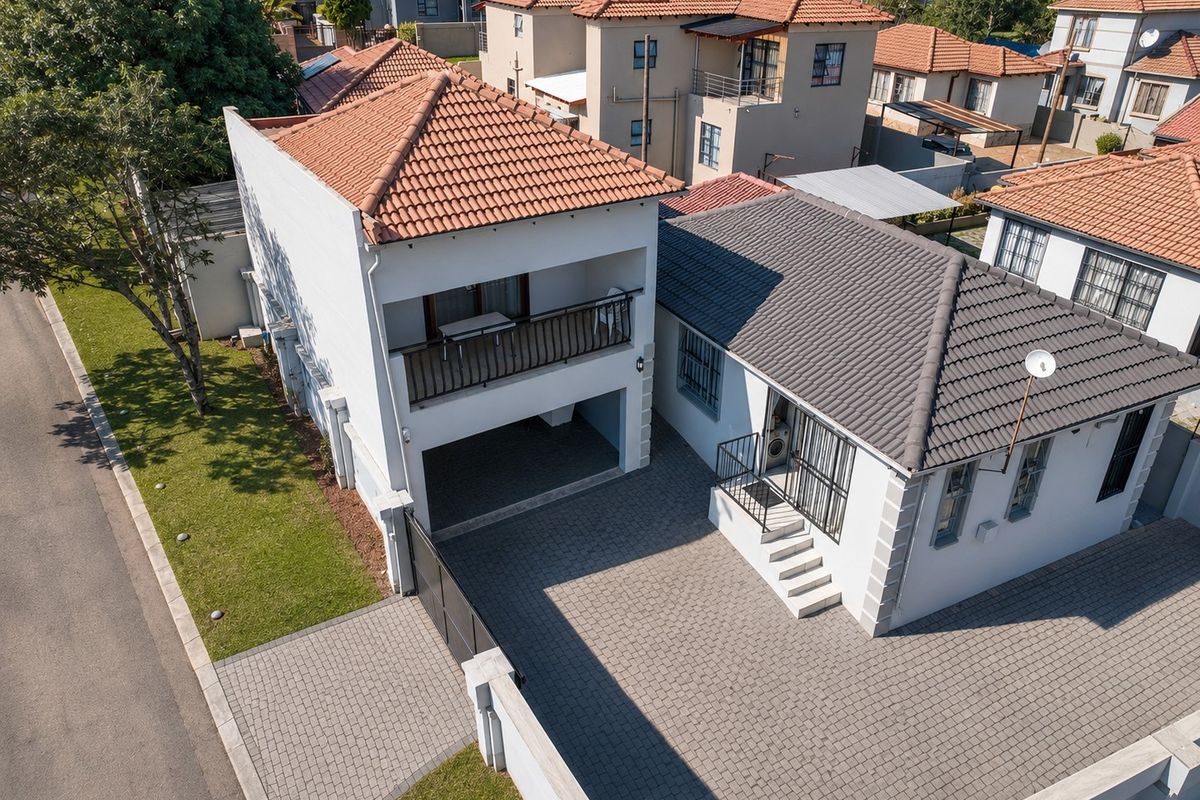 Aerial view of a residential property featuring a paved driveway, tiled roof, and a balcony, situated within a suburban neighborhood.