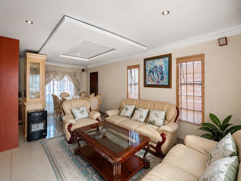 An open-plan living and dining area featuring tiled floors, a recessed ceiling with downlights, and wooden window blinds.