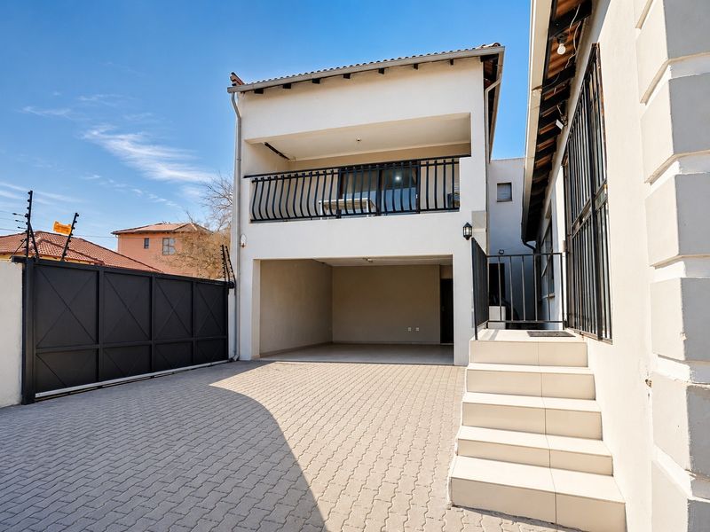 Front exterior view featuring a paved driveway, secure metal gate with electric fencing, a covered parking area, and an upper-level balcony with metal railings.
