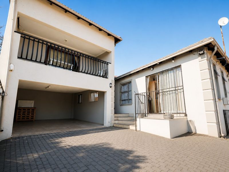 Exterior view of a multi-level residential property featuring a paved driveway, covered garage space, and an upper-level balcony with metal railings.