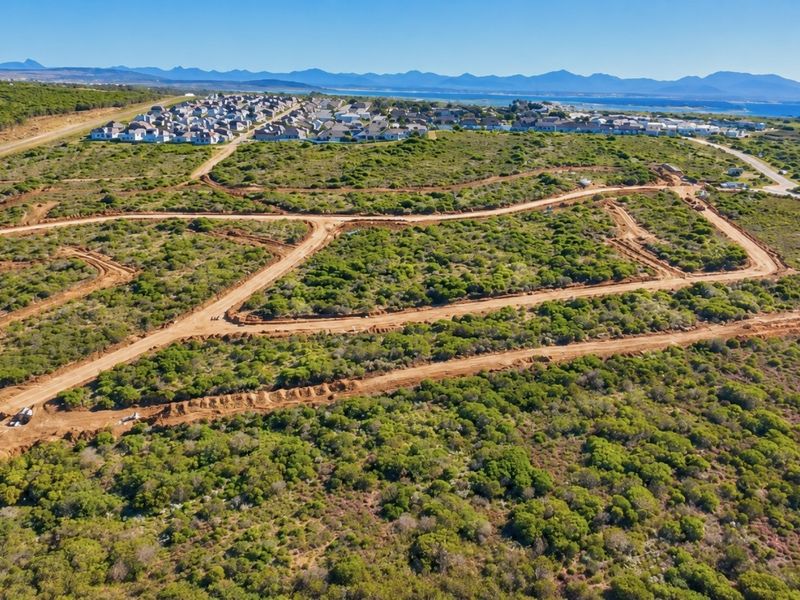 Aerial view of a large residential development site featuring cleared dirt roads and natural coastal vegetation with distant mountain and ocean views.