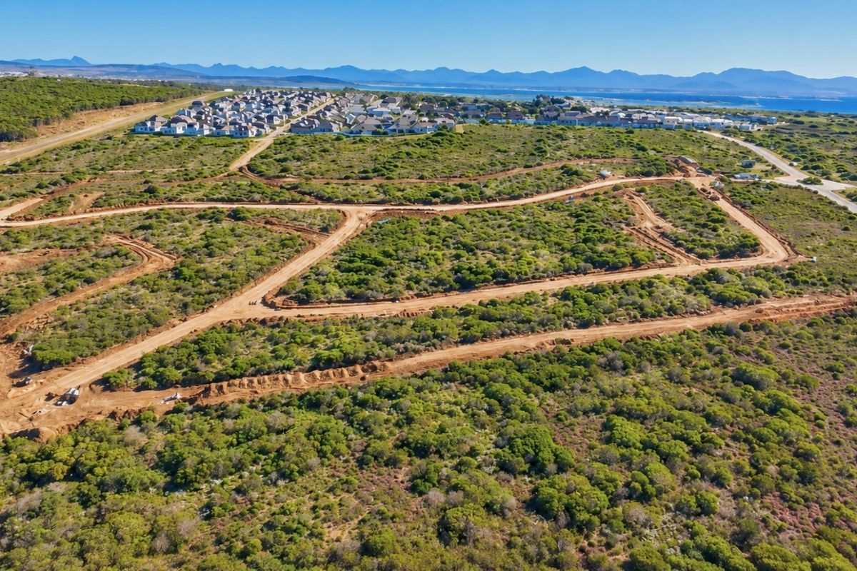 Aerial view of a large residential development site featuring cleared dirt roads and natural coastal vegetation with distant mountain and ocean views.