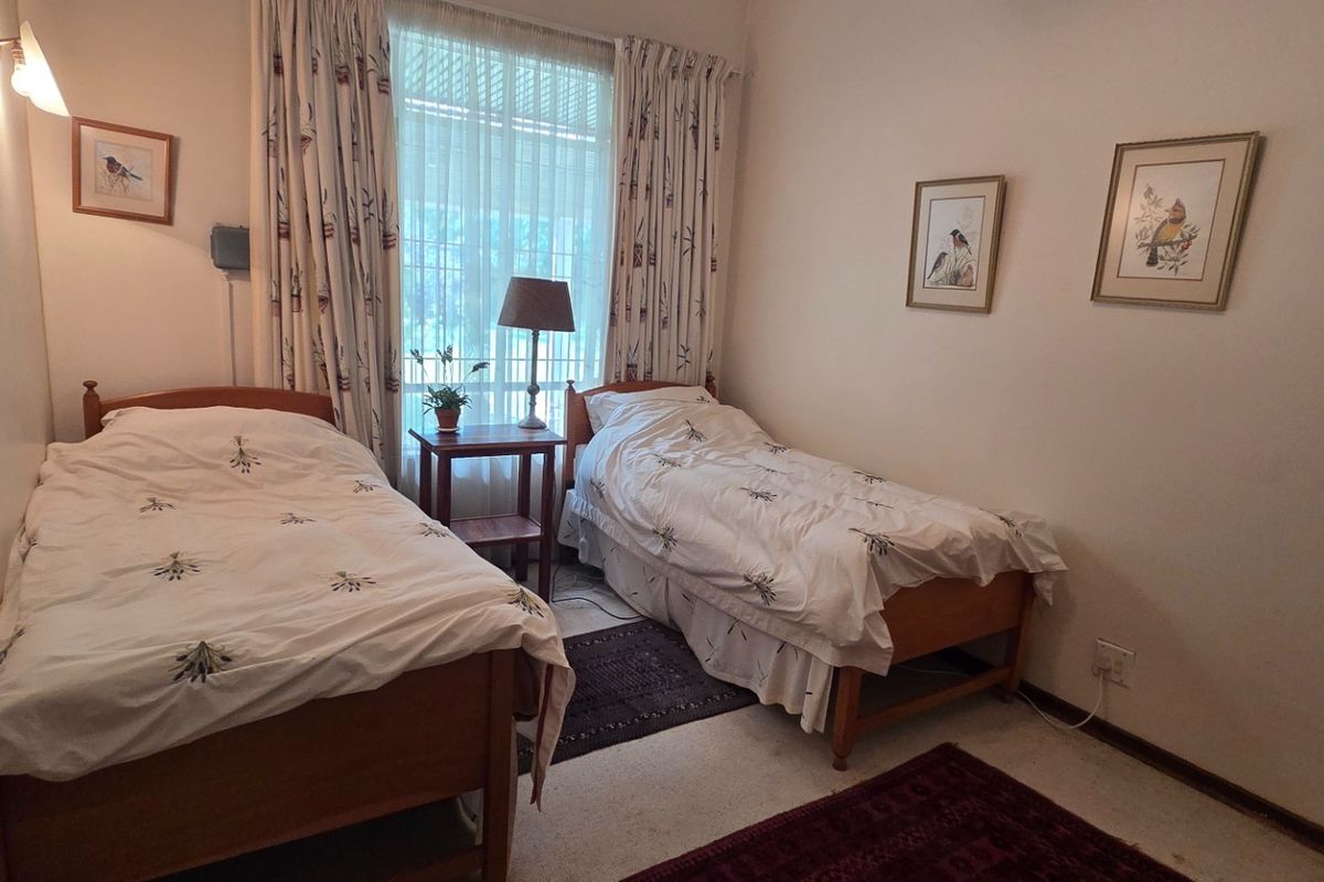 A functional bedroom featuring neutral walls, carpeted flooring, and a large window with curtains, providing a comfortable space for rest.