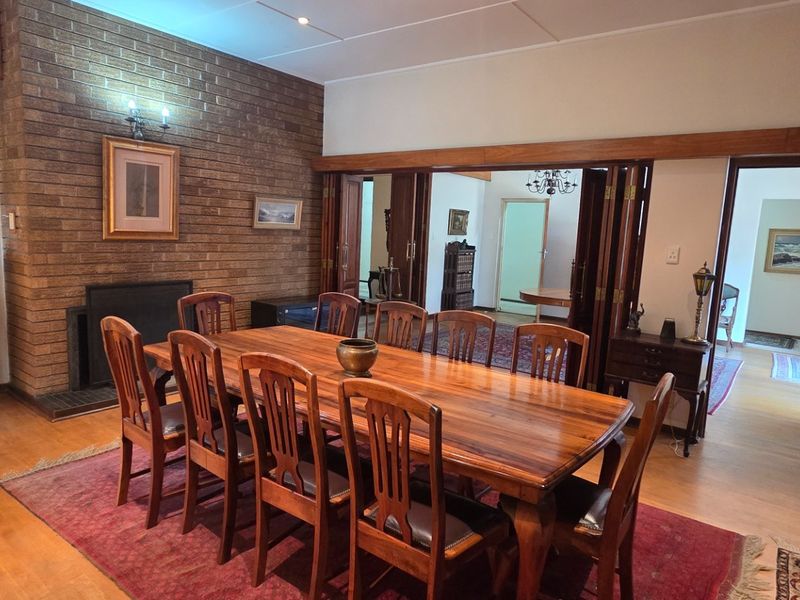 Spacious dining room featuring a prominent brick fireplace, warm timber flooring, and classic timber folding doors connecting to adjacent living areas.