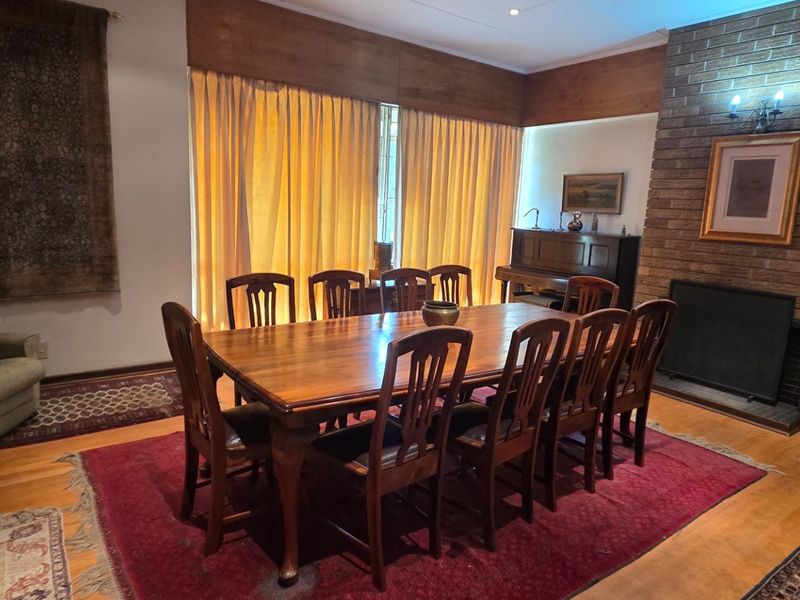 Spacious dining room featuring a prominent brick fireplace, hardwood flooring, and large windows with timber pelmets, offering a classic and warm atmosphere.
