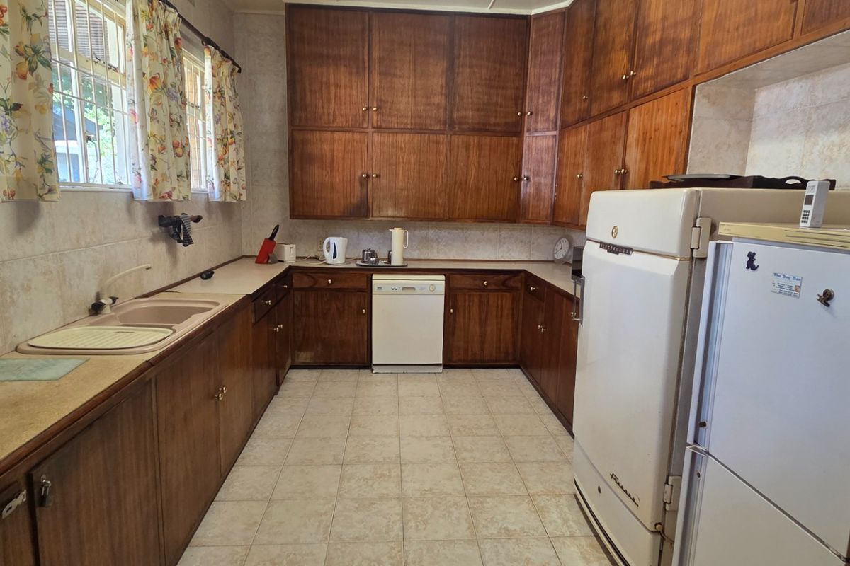 A functional kitchen featuring extensive wooden cabinetry, laminate countertops, tiled flooring, and a double basin sink, offering significant potential for modern renovation.