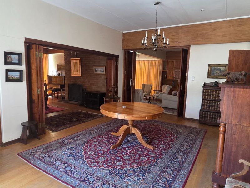 Spacious living area featuring hardwood flooring, timber folding doors, and an exposed brick fireplace, connecting multiple living spaces with a traditional aesthetic.