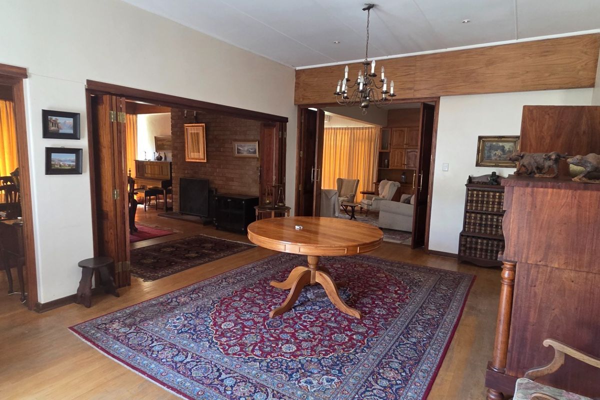Spacious living area featuring hardwood flooring, timber folding doors, and an exposed brick fireplace, connecting multiple living spaces with a traditional aesthetic.