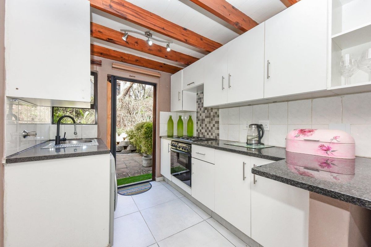 A functional kitchen featuring white cabinetry, granite countertops, built-in oven, gas hob, and exposed timber ceiling beams with direct access to the rear patio.