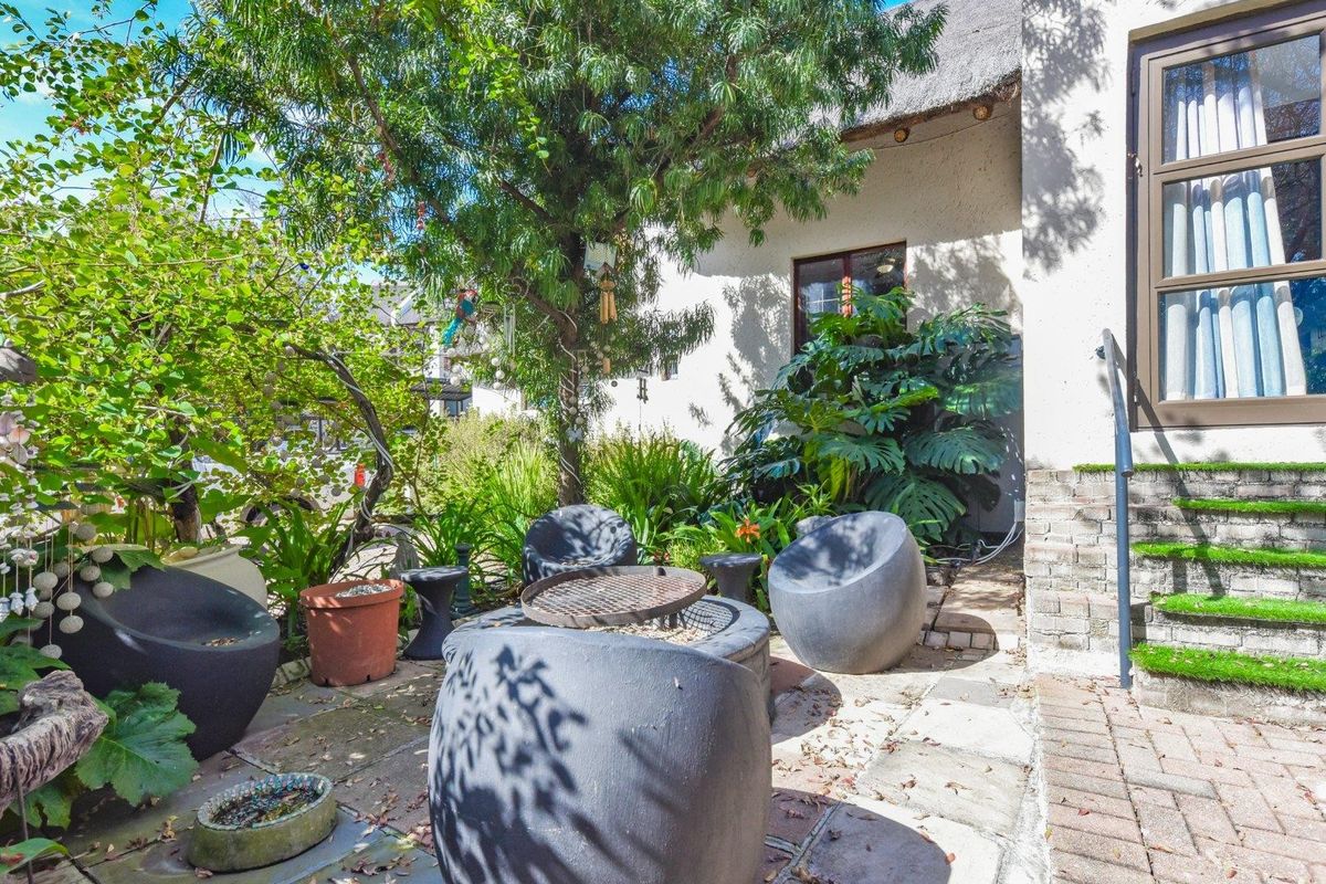 A private rear patio area featuring paved flooring, brick steps leading to a sliding door, and a traditional thatched roof overhang.