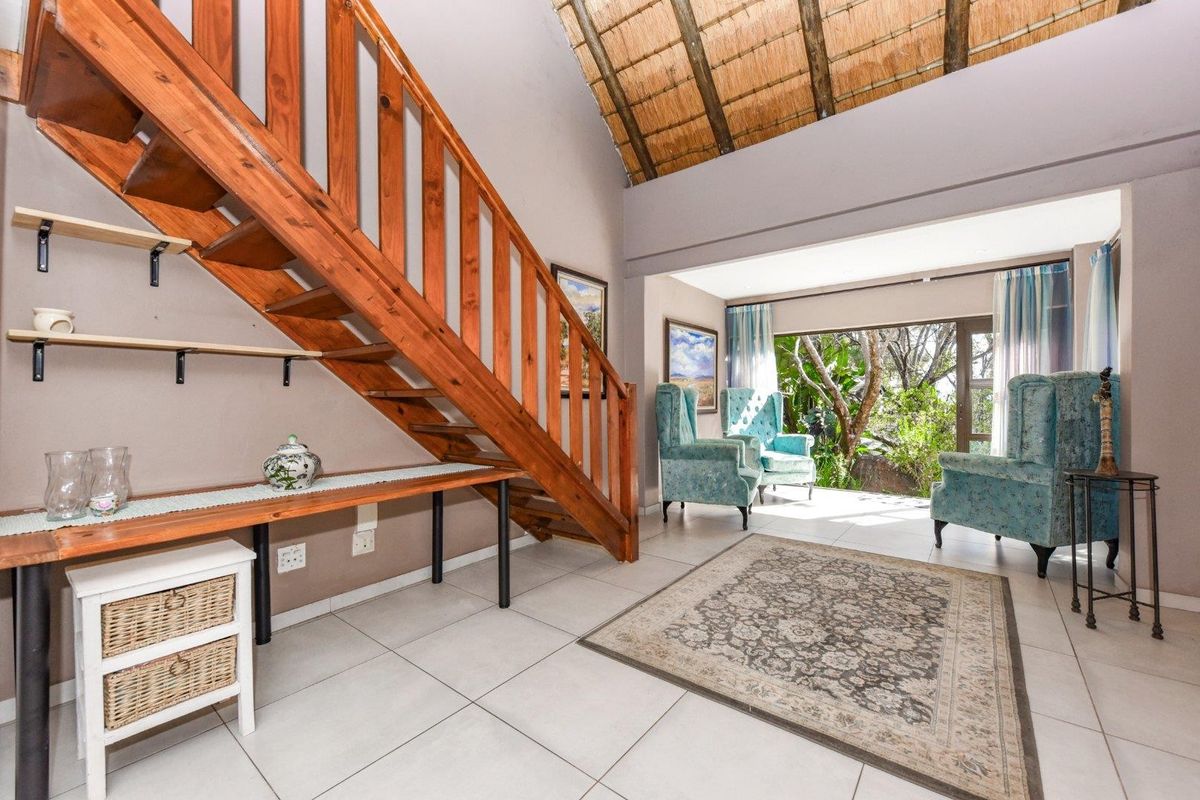 Spacious living area featuring a timber staircase, high thatched ceiling, and large sliding doors opening to a lush garden view.