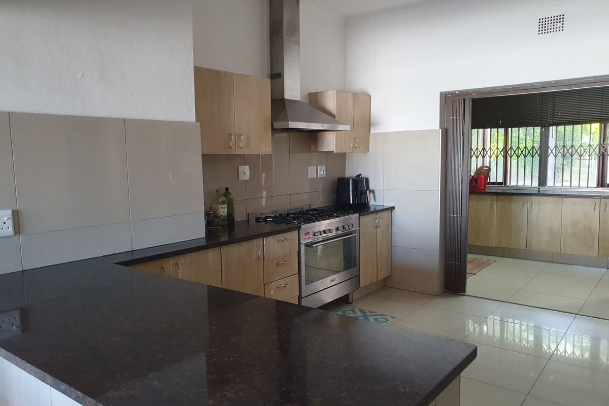 A functional kitchen featuring granite countertops, stainless steel gas stove, extractor fan, and ample built-in cabinetry with neutral tiled finishes.