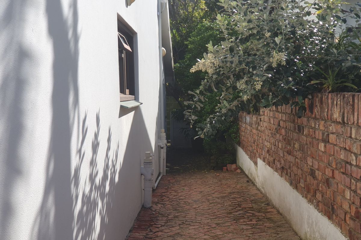 A narrow side passage featuring brick paving, a brick boundary wall, and external wall finishes.