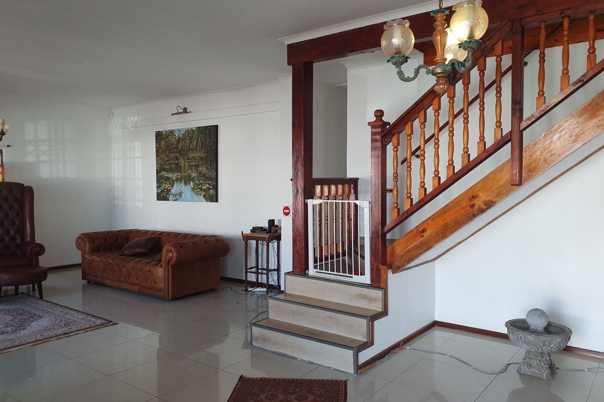 Spacious living area featuring a prominent wooden staircase with a balustrade, tiled flooring, and a classic chandelier, offering a traditional interior layout.